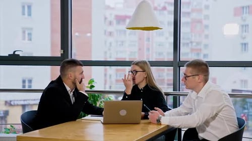 Little meeting of colleagues in the office. People sit at desk, talk and use modern gadgets.