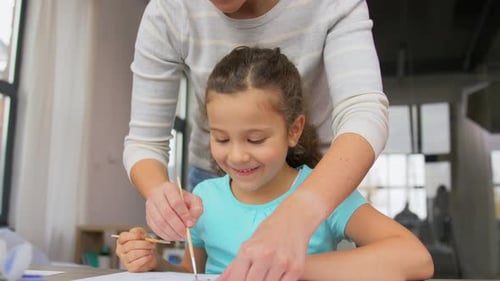 Mother helps young girl painting wooden figures indoors