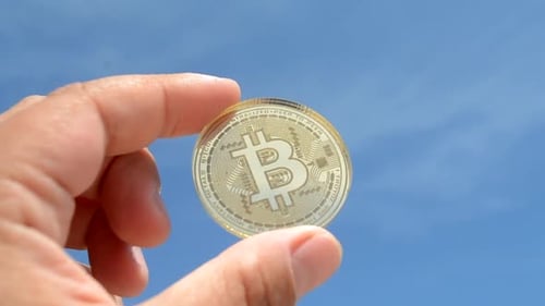 Hand Holding Gold Bitcoin Against Blue Sky