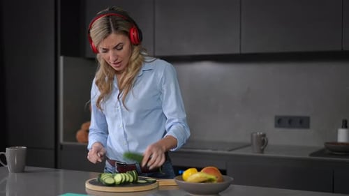 Woman with Headphones Cuts Cucumber in Kitchen