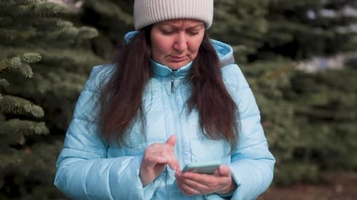 Frown Woman Typing Message Chatting in Smartphone Outdoors in Fir Tree Park