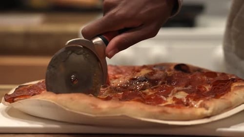 Slicing a freshly baked pepperoni pizza with a pizza wheel hot out of the oven - side view