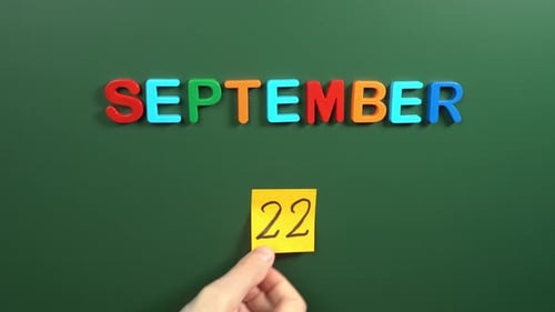 Hand sticking a sticker 22 September calendar day on school board. 22 date of September. Twenty