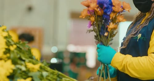 Florist woman in uniform preparing bouquets of colorful flowers in an industrial flower shop.