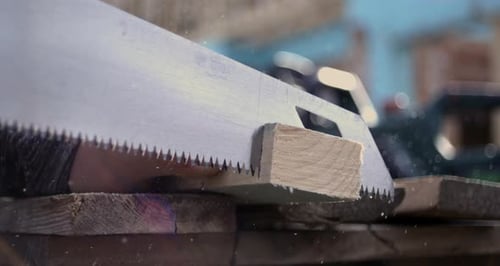 Hand saw cutting into wood plank, sawdust particles in air, detailed view of wood texture, slow