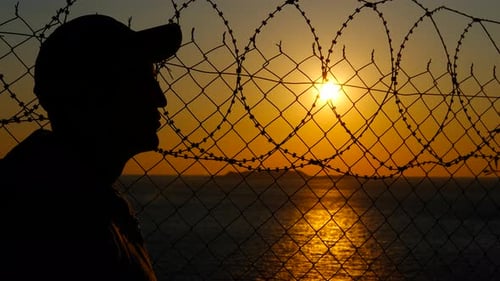 Man Observing Sunset Behind Barbed Wire Fence