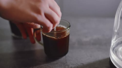 Close Up Of Hand Stirring Hot Coffee In Glass Mug