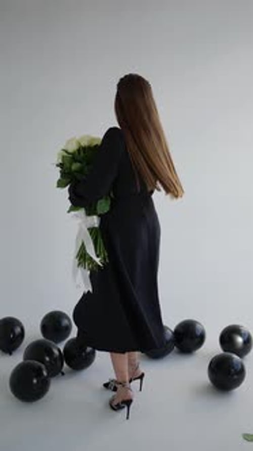 Elegant Woman Holding Flowers Among Black Balloons
