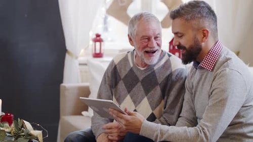 Mature Man and Senior Father Indoors at Home at Christmas, Using Tablet