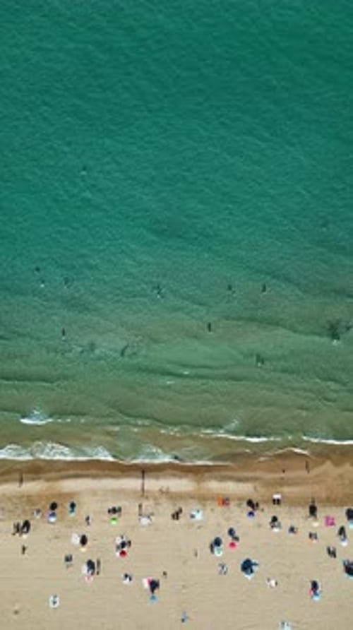 Aerial drone view of the buildings along the coastline with people relaxing on the beach in Alicante