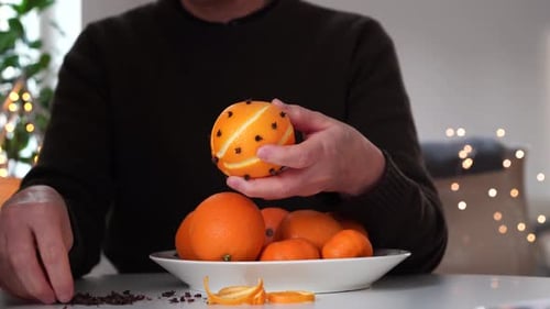 Oranges Pomander aux clous de girofle faites par une femme à table avec bokeh en arrière-plan.