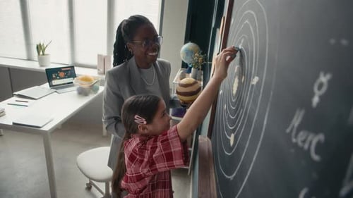 Girl Draws Solar System on Blackboard in Classroom