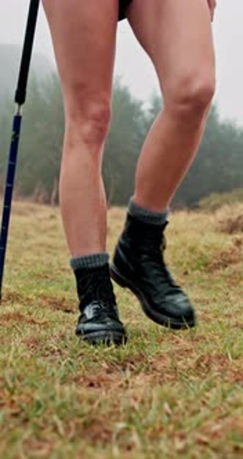 Person, legs and hiker with walking stick on grass field for adventure, journey or outdoor trip