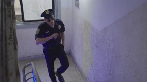 Police officer patrols residential building, cautiously climbing a staircase.