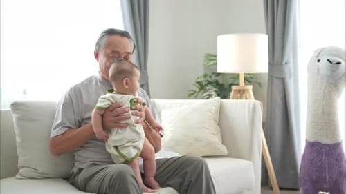 Grandfather Cradling Infant on Couch Indoors