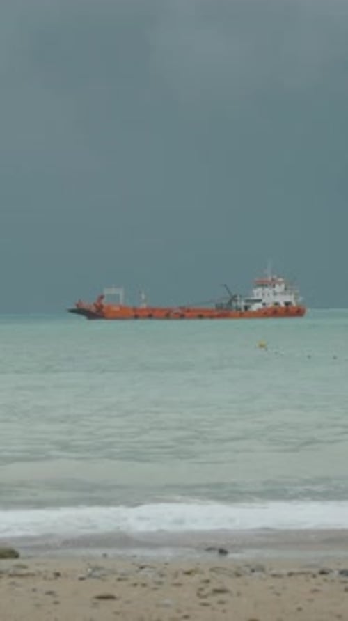 Dark sky, and a storm is approaching from the sea. A red ship sways on the waves
