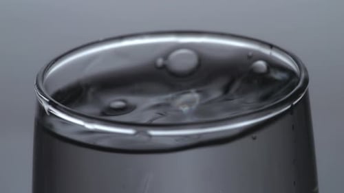 Primer plano del cubo de hielo que cae en un vaso de agua potable sobre el fondo de pantalla blanco claro