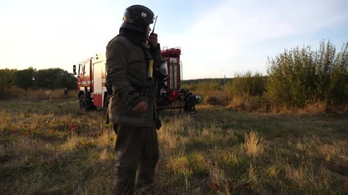 Professional Fireman in Full Equipment Talking on Walkietalkie on Place at Fire Near a Big Red Truck