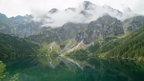 mountain lake against the backdrop of high mountains and fast-moving clouds, time-lapse sun glare