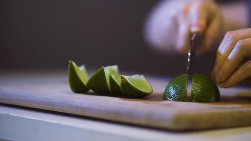 Hands Cutting Lime into Wedges on Cutting Board