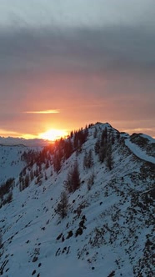 Atemberaubender Blick auf den schneebedeckten Sonnenuntergang in den Bergen, aufgenommen am Winterabend
