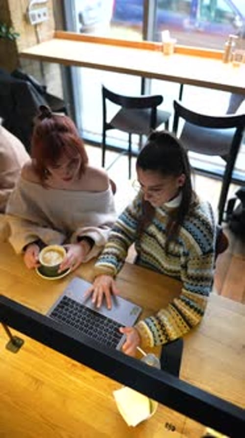 Young Female Friends Working Together with Laptop Computer at Outdoor Cafe