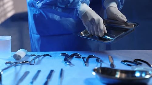 Doctor with different surgical tools at table in hospital, closeup