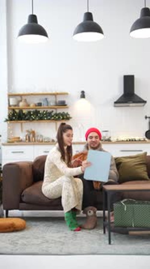 With Their Dog a Young Man and a Girl Spend Time Near the Christmas Tree in Their Apartment