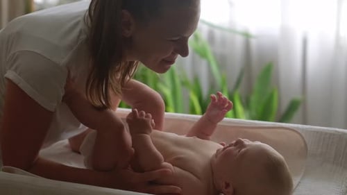 Mom and Infant Baby at Home Young Mother Leans Over Changing Table Gently Kissing Her Baby Forehead