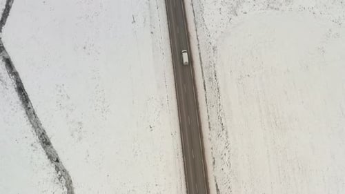 Top down aerial drone view of a white van driving on a road in snow covered winter day. Vehicle purs