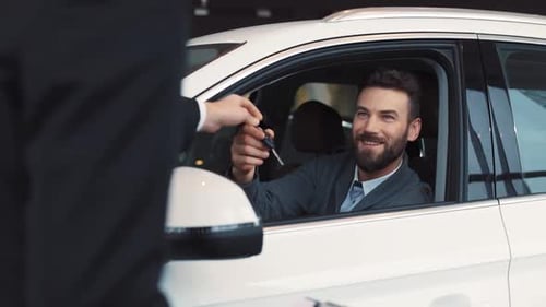 Young Handsome Businessman Sitting on Driver's Seat in White Car Seller Giving Keys to Buyer of Car