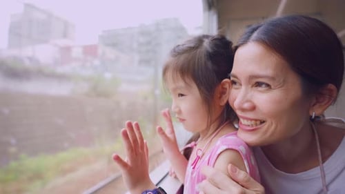 Una joven asiática mira a la vista mientras viaja en el tren con su madre.