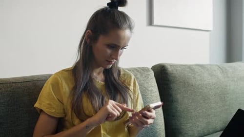 Low angle view of caucasian woman sitting on sofa and browsing phone. Shot with RED helium camera in