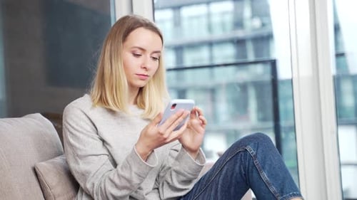 Woman Smiling While Using Smartphone in Apartment