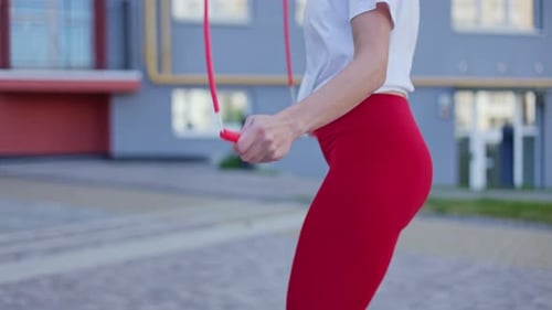 Side View of Sports Female in Midjump While Using Red Skipping Rope Outdoors