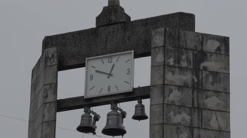 Drei kleine Glocken mit einer großen weißen Uhr an der Spitze einer christlichen Kirche