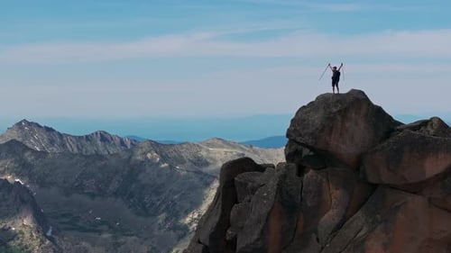 A Young Man Raises His Arms Victoriously at the Top of the Mountain