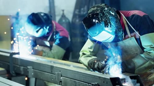 Professioneller Schweißer, der in der Fabrikwerkstatt der Fabrik arbeitet, mit einem männlichen Techniker beim Schweißen