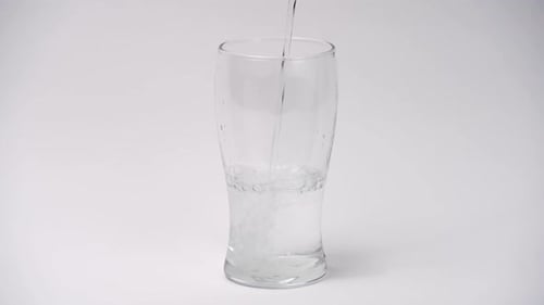 Cámara lenta y de primer plano de verter agua en un vaso sobre fondo blanco