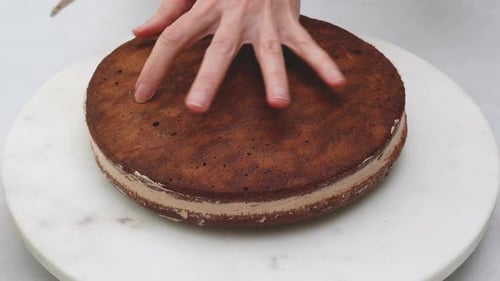 Person Frosting a Layer Cake on Marble Surface