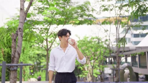Asian young businessman drinking a cup of coffee while walking in city.