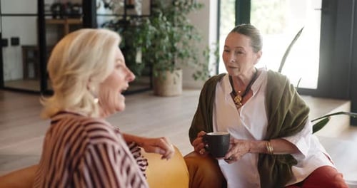 Two Senior Women Chatting Indoors with Coffee Mugs