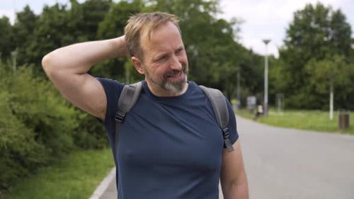 A Handsome Middleaged Caucasian Man with a Backpack Walks in a Park and Looks Around Then Smiles