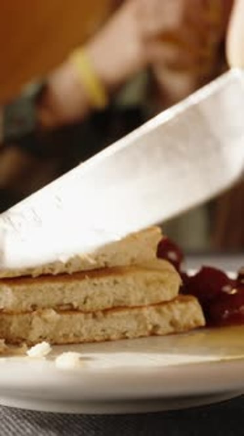 Vidéo verticale. Couper un morceau de crêpes et y étaler du miel, ainsi que des cerises.