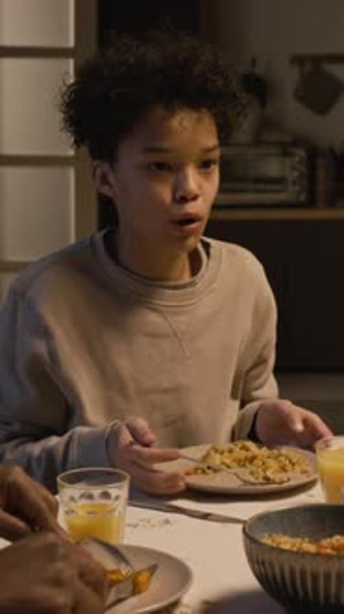 Adolescente sonriente que pide más comida disfrutando de una cena con su familia Vertical