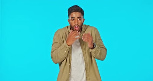 Scary, face and a man with fear of a hit isolated on a blue background in a studio