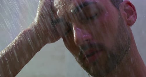 Close up of an young handsome man is taking a hot relaxing shower in a luxury wellness center.