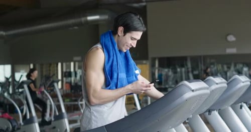 Portrait of a guy in a gym while resting between a workout and the other uses his phone to watch s