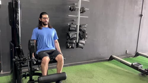 Homem latino com barba e cabelo comprido em equipamento de cadeira extensível.