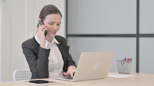 Woman working with laptop and smartphone in office